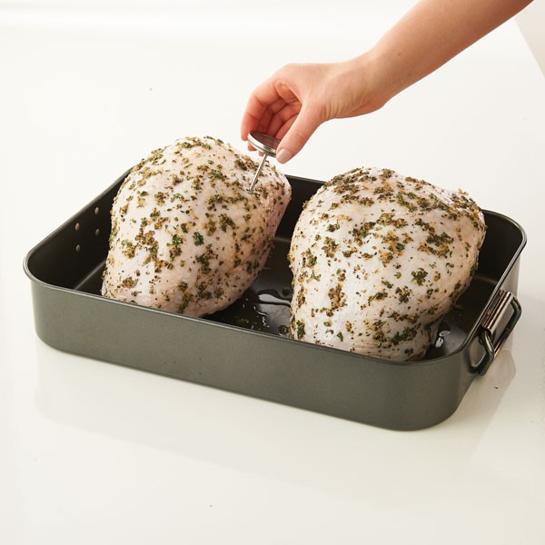 Seasoned turkey breasts in roasting pan inserting thermometer