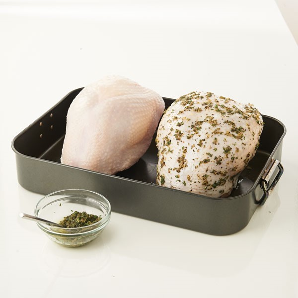 Raw turkey breasts in roasting pan with one covered in spices